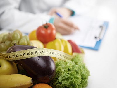 Healthy nutrition concept. Close-up of fresh vegetables and fruits with measuring tape lying on doctor's desk.